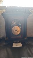 Full view of dark wood mantel clock showing rectangular shape, glass door, decorative metal around clock face, and ornate feet.