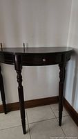 Front table made of dark cherry wood with semi-circular top and one drawer, supported by four turned legs, positioned against wall.
