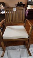 Front view of large wooden rocking chair with white cushion, vertical slat back and curved rocker legs.