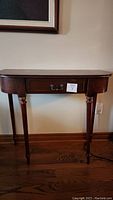 Front view of small dark wood table with single drawer and four legs, showing general shape, drawer face with handles, and floor placement.