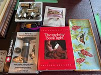Multiple items on table including Birks napkin rings, chrome napkin rings, photo bracelet, Itty Bitty book light, wine saver, and ceramic tray.