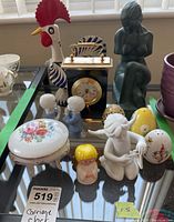 Photo showing carriage clock, rooster figurine, female figurine, small child and angel figurines, salt and pepper shakers, and porcelain trinket box arranged on table.