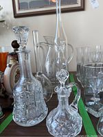 Front view showing two crystal cut-glass decanters with stoppers, tall etched decanter, and a clear glass pitcher among surrounding glassware.