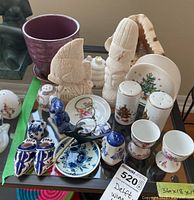 View of lot showing Delft ceramics including salt and pepper shakers, small plates, wine holder figurine, carved figures, butterflies, and a purple ceramic pot.
