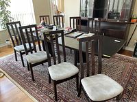 Eight high backed wood dining chairs with padded fabric seats arranged around a table in living space, showing the set quantity and general condition.