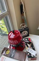 Red metal fondue pot with burner stand, forks, and box of forks, a boxed Philips electric corkscrew, black leatherette clock, and two pairs of cross country ski poles leaning against a wall
