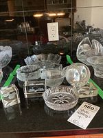 Photo of multiple clear glass bowls and figurines including swans, owl, and etched designs on a dark surface