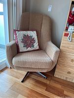Front angle of beige textured upholstered swivel chair with decorative poinsettia cushion on seat.