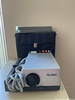 Rollei slide viewer with power cord and carrying case. Side view showing focus knob and control buttons on top.
