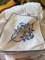 Photo of white linen tea cloth with cutwork and blue embroidered design.