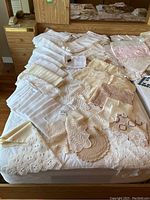 Photo showing a collection of linen tablecloths, embroidered and crocheted doilies, and dinner napkins arranged on a bed.