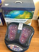 Photograph of the Technomedic Deluxe Infrared Vibration Foot Massager with box in background, showing footpads and control panel clearly.
