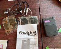 Photo showing the ProActive TENS device, four electrodes (two sealed in plastic, two attached to cables), and the user manual.