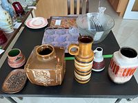 Overview of six pottery items on black table including vases and a decorative plate