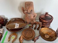 Photo shows a collection of woodware including a carved wooden tray, elongated bowl, ice bucket with lid, carved wooden figurine, and other decorative items like a glass bowl and ceramic figure.