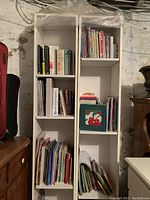 Two tall white bookshelves filled with books, displayed side-by-side against a basement wall, showing adjustable shelves and item condition.