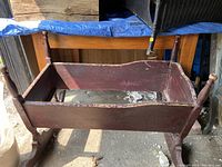 Photo of large brown wood antique cradle missing the bottom panel from an angle