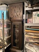 Full view of antique grandfather clock showing wooden frame, clock face, and pendulum through glass pane.