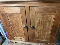 Front view of antique wood cabinet showing two paneled doors with round wooden knobs and visible wood grain.