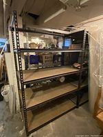 Side view of a large black metal industrial shelving unit with particle board shelves in a basement or storage setting.