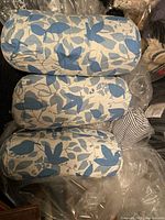 Three oval blue and white outdoor cushions with leaf patterns, stacked side-by-side on a surface covered in plastic.