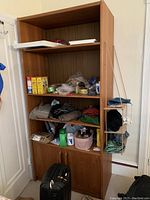 Bookcase showing three open shelves including miscellaneous items and two closed drawers at the bottom. Positioned next to a wall with a hanging fabric organizer.