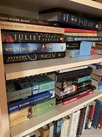 Three shelves showing a variety of cookbooks, fiction, and non-fiction books stacked horizontally and vertically.