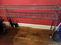 Front view of the metal kitchen shelf rack against a red wall and wooden floor