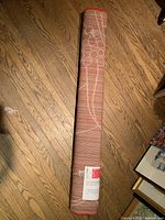 Rolled up pink carpet with subtle white flower design laid on hardwood floor.