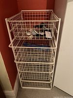 White metal sliding basket system with four wire mesh sliding baskets installed in a corner space.
