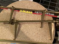 Brass metal stand frame with angled support legs and mounting flanges on circular wooden surface.
