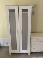 Front view of a white wooden wardrobe with two frosted glass panel doors and white vertical handles against a pale wall.