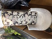 Top-down view of the white wicker lounge chair showing floral cushion with tears and damage to the cushion.