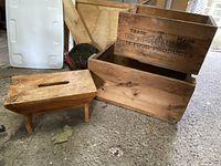 Photo showing two wooden boxes, one stacked on the other, and a small wooden stool on a concrete floor.