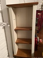 Full front view of wood shelf unit showing three brown wood shelves and white frame, missing one shelf