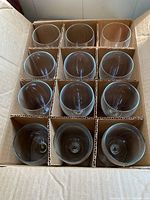 Box containing 12 plain wine glasses separated by cardboard dividers; 11 glasses of the same large size and 1 smaller size glass.