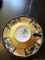 Close up of the bottom of a teacup showing the Wedgwood & Co. stamp with the name Nanette and yellow and black floral pattern.