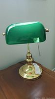 Full view of brass based bankers lamp with green glass shade placed on wooden table.