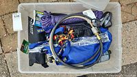 Overhead view of all items in plastic storage bin visible: propane hose attachments, purple rope, headlamps, Katadyn water filter pouch.