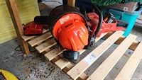 Overview of chainsaw, battery, charger, and helmet arranged on wooden pallet