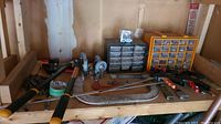 Photo showing overall lot on wooden shelf including branch trimmer handles, clamps, caster wheels, chain coils, tape roll, and compartment boxes with hardware.