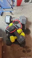 Pile of various free weights including hexagonal black York dumbbells and smaller neoprene coated dumbbells in yellow and green, all heavily used and dusty.
