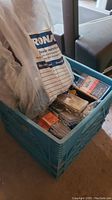 Photo of blue plastic milk crate filled with assorted screws and nails in packaging and loose form under a plastic bag.