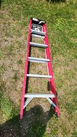 Full top-down view of six foot step ladder on grass showing entire length and red frame with silver steps.