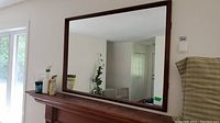 Full front view of rectangular teak framed mirror above wooden mantel