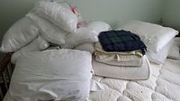 Wide view of bed with piled pillows, folded blankets, mattress protector and sheets