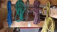 Four coils of rope and a metal chain with lock hanging on a wooden beam.