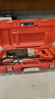 Red plastic carrying case open showing Milwaukee Sawzall reciprocating saw inside with cord coiled