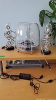 Photo showing both transparent satellite speakers, dome-shaped subwoofer, and accessories on table