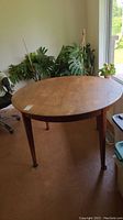 Full view of round teak table on tapered legs in unfurled configuration